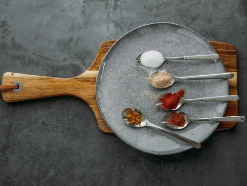 Pommesgewürz auf Löffeln und Teller vor dunklem Hintergrund.