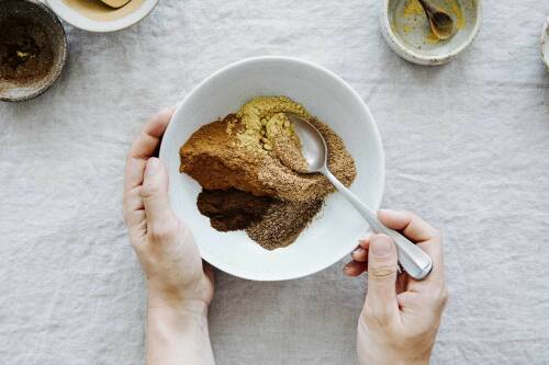 Pumpkin Spice Würzmischung in Schüssel mit Händen und Löffel vor weißem Hintergrund.