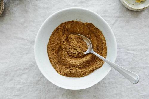 Pumpkin-Spice Gewürzmischung in weißer Schüssel mit Löffel vor hellem Hintergrund.