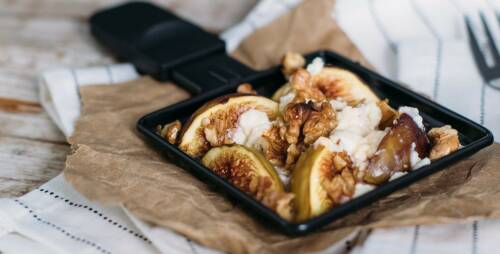 Raclette-Pfännchen gefüllt mit Feigen, Ziegenkäse und Walnüssen. Darunter ein Stück Backpapier. Von oben seitlich fotografiert.