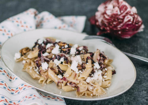Ein leckeres herbstliches Gericht: Pasta mit Radicchio, Walnüssen und Feta auf einem Teller, daneben eine Gabel. Von der Seite fotografiert.
