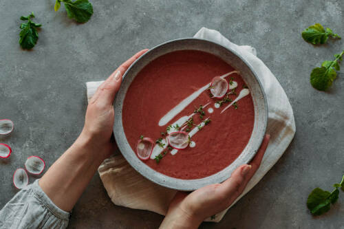 Radieschen Suppe in Teller und Händen mit Kräutern vor dunklem Hintergrund.