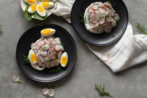 Radieschensalat mit Eiern in dunklen Tellern vor hellem Hintergrund.