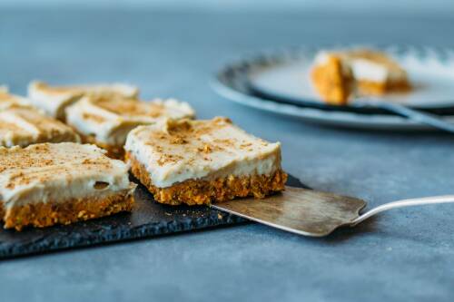 Raw Carrot Bites mit veganem Frosting auf Schieferplatte vor hellem Hintergrund.