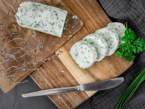 vegane Kräuterbutter in Scheiben geschnitten auf einem Holzbrett und Messer