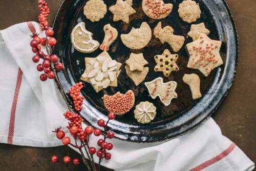 Vegane Butterplätzchen mit Zuckerguss auf einem Teller: Sterne, Monde, Vögel. Von oben fotografiert.