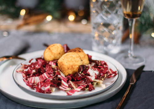 Panierte Risottobällchen auf einem Bett aus knackigem Radicchio. Von oben-seitlich fotografiert.