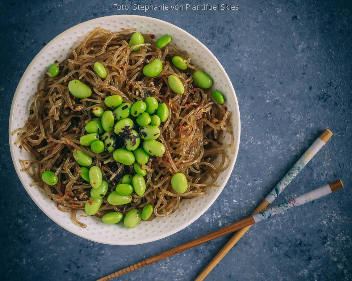 Weißer Teller mit rohen Kelp-Nudeln, Edamame und Esstäbchen