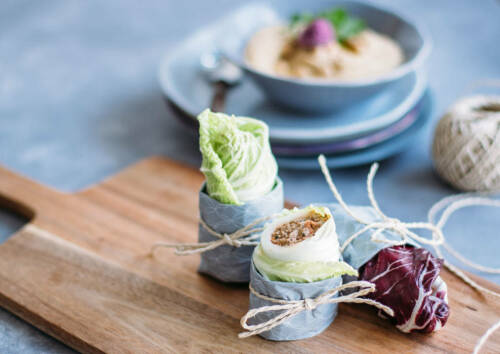 Salat-Wraps zu kleinen Bündeln geschnürt auf einem Holzbrett, dahinter ein Dip, von vorne fotografiert
