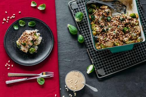 Rosenkohl Auflauf mit Tahin-Soße auf Teller und Auflaufform vor rotem Hintergrund.