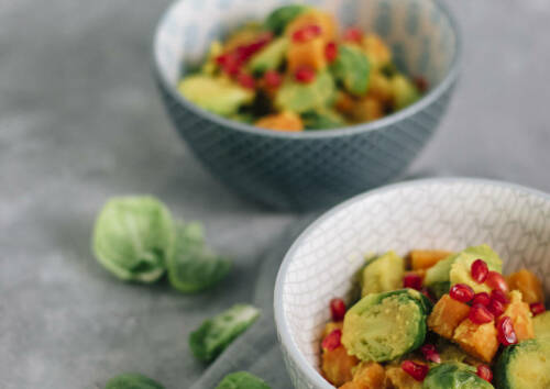 Leckeres Curry mit Rosenkohl in einer Schüssel vor grauem Hintergrund, von vorne fotografiert.