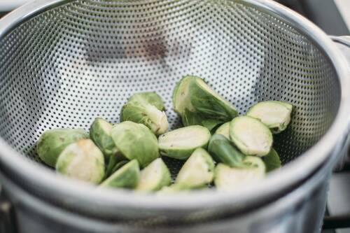 Halbierter Rosenkohl in einem silbernen Sieb.