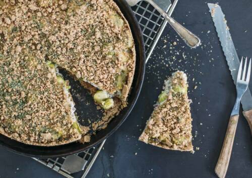 Leckere Rosenkohlquiche – frisch aus dem Ofen auf einem Gitter, daneben Messer und Gabel. Von oben fotografiert.