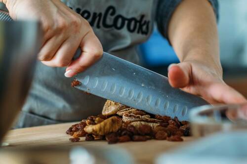 Rosinen mit Messer und Händen gehackt auf Schneidebrett vor hellem Hintergrund.