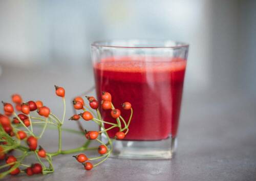 Ein Glas firsch gemachter Rote-Bete-Karottensaft auf einer grauen Anrichte.