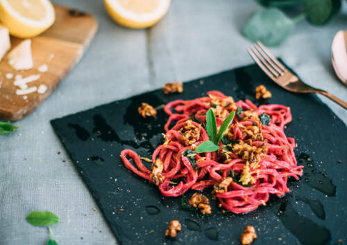 Knallig rote Nudeln aus rote Bete mit Salbei auf einer Schieferplatte, von oben fotografiert.