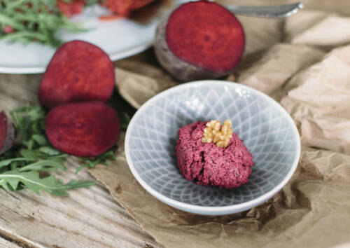 Frisch gemachtes Pesto aus roter Bete und Walnüssen in einer blauen Schale. Im Hintergrund: aufgeschnittene rote Bete.