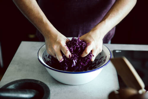 Geraspelter Rotkohl wird in einer weißen Schüssel geknetet.