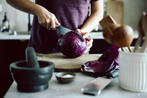 Ein Rotkohl wird mit einem großen Messer auf einem Holzbrett durchgeschnitten.