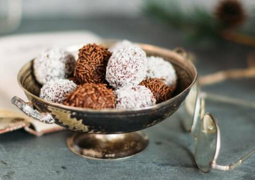 Zweierlei Rumkugeln in Schokostreuseln und Kokosmantel in einer Schüssel. Von der Seite fotografiert.