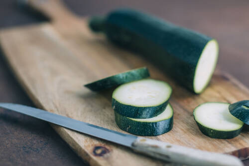 Aufgeschnittene Zucchini auf einem Schneidebrett mit einem Messer von oben-seitlich