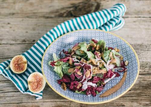Salat mit Nüssen, Radicchio und Feigendressing in blau gemusterter Schale. Daneben Feigen, auf Holzuntergrund fotografiert.