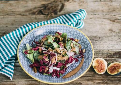 Salat mit Feigendressing in gemusterter Schüssel, daneben Geschirrtuch und Feigen auf einer Holzplatte, von oben fotografiert
