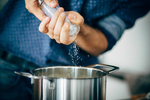 Mann streut Salz in Topf