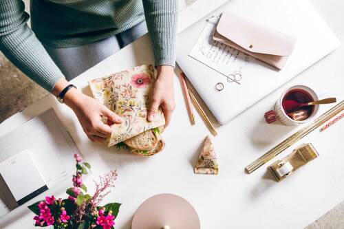 Ein belegtes Brot in einem Bienenwachstuch von Little Bee Fresh. Eine am Schreibtisch sitzende Frau hält es in der Hand.