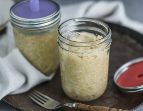 Sauerkraut in Glas neben Gabel vor dunklem Hintergrund.