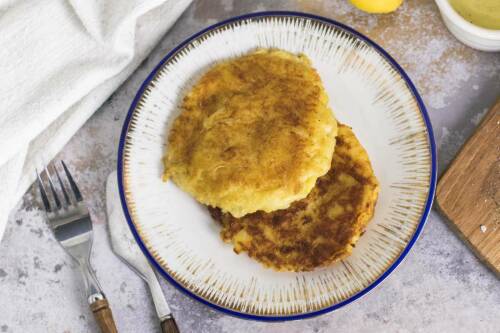 Sauerkraut Kartoffelpuffer auf weißem Teller neben Besteck vor hellem Hintergrund.