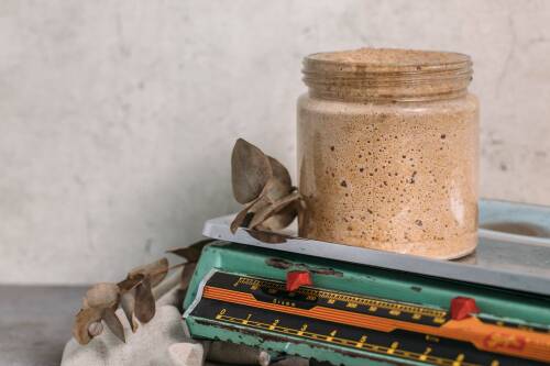 Sauerteig in Glas auf alter Waage vor hellem Hintergrund.