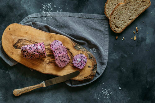 Schalotten-Rotwein-Butter auf Schneidebrett neben Bauernbrotscheiben vor dunklem Hintergrund.