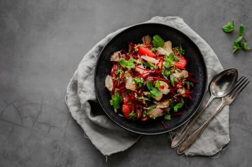 Scharfer Zitrussalat in schwarzem Teller neben Besteck vor dunklem Hintergrund.