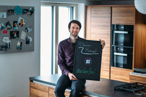 Junger Mann hält ein Schild mit der Aufschrift "Diesen Monat zuckerfrei"