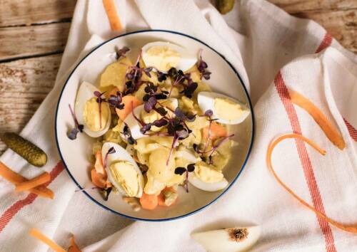 Schlesischer Kartoffelsalat mit Ei und Karotten, darüber lila Kresse. Von oben fotografiert.