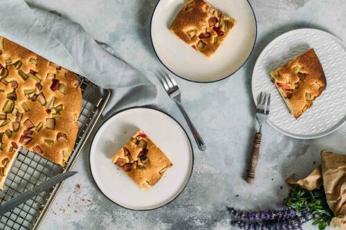 Schneller Rhabarberkuchen auf Blech und Tellern vor hellem Hintergrund.