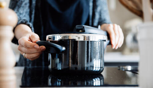 Schnellkochtopf mit Händen auf Herd vor hellem Hintergrund.