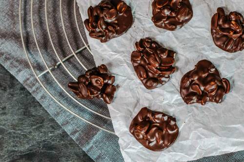 Schoko Bites mit Erdnüssen und Cranberries uf Butterpapier vor dunklem Hintergrund.