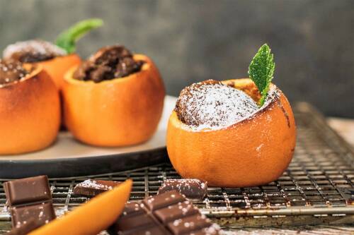 Schokokuchen in Orangenschale neben Schokolade mit Puderzucker vor dunklem Hintergrund.