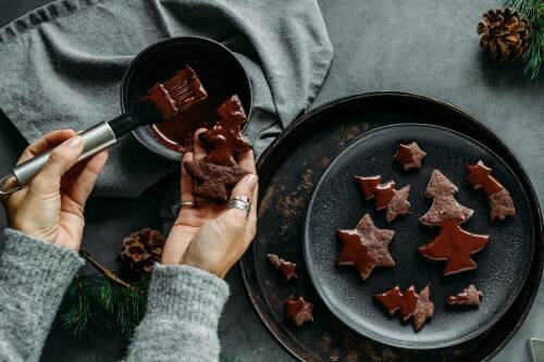 Schokoladige Zucchiniplätzchen mit Schokoguss auf schwarzem Teller mit Händen vor dunklem Hintergrund.