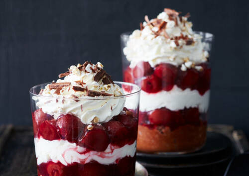 Leckeres Mini-Dessert im Glas mit Kirschen, Sahne und Schokolade, von der Seite fotografiert.