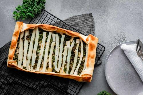 Schwarzwurzel Galette auf Gitter neben Teller vor hellem Hintergrund.