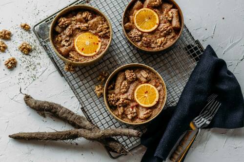 Schwarzwurzelauflauf mit Walnüssen in Schüsseln auf Blech neben Besteck vor hellem Hintergrund.