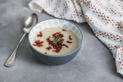 Schwarzwurzelsuppe in blauer Schüssel neben Löffel vor hellem Hintergrund.
