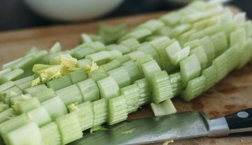 Stangensellerie aufgeschnitten auf einem Holzbrett, davor liegt ein Messer. Nahaufnahme von der Seite.