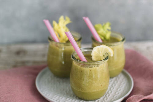 Sellerie-Matcha-Smoothie in Gläsern mit Zitrone und Strohhalmen vor hellem Hintergrund.