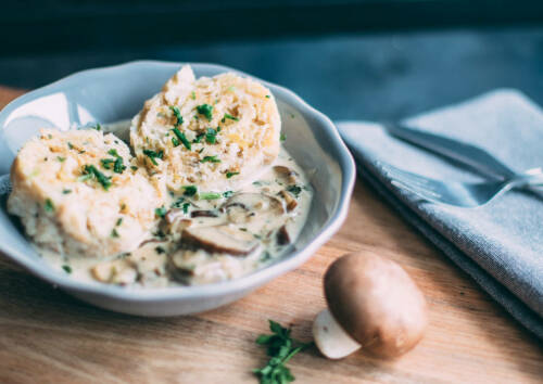 Semmelknödel in Champignon-Rahm mit Petersilie in einer Schale, von oben fotografiert.