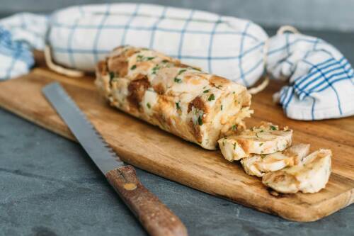 Serviettenknödel kann man ganz leicht selbst herstellen und dann einfach nach Bedarf abschneiden und portionieren. Zu sehen ist eine Rolle Serviettenknödel, angeschnitten auf einem Schneidebrett.
