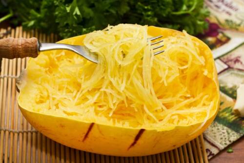 Spaghettikürbis mit Gabel und Petersilie vor hellem Hintergrund.